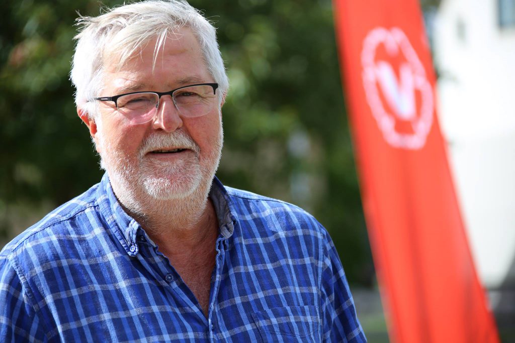 Anders Lövgren med grönska och V-fana i bakgrunden